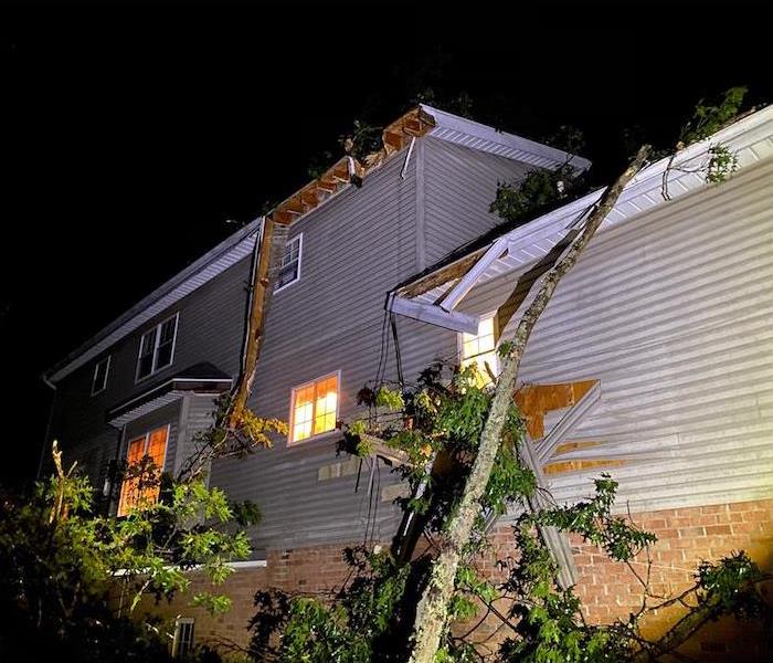 Dramatic night shot of a home with visible roof damage from a recently storm and fallen debris